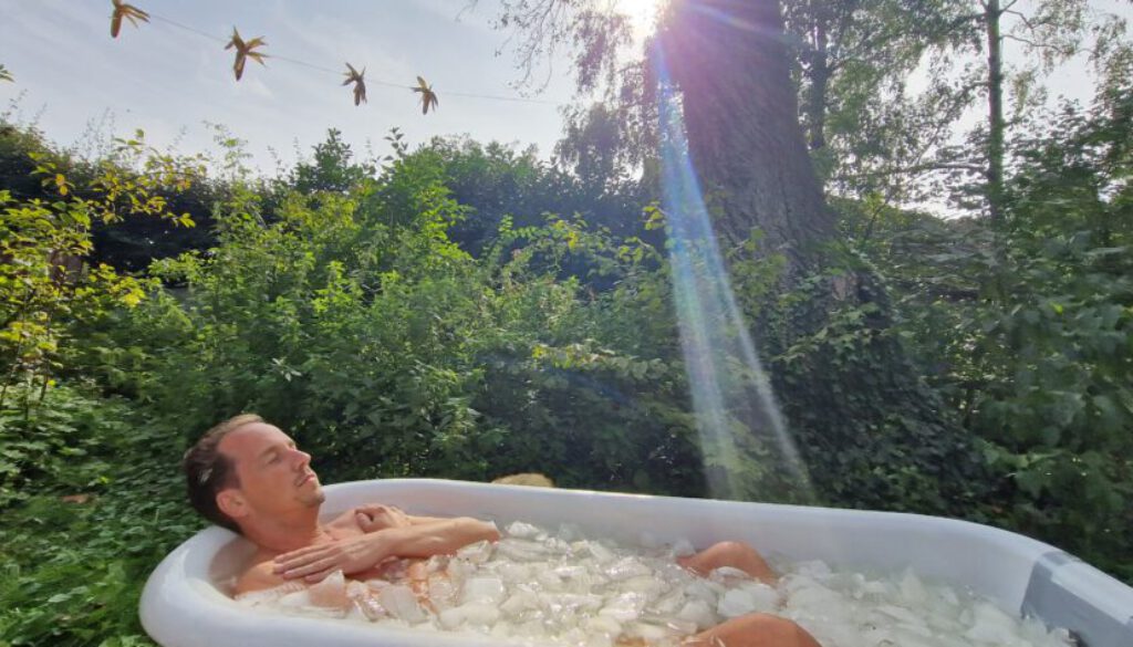 Een man ligt in een ijsbad midden in de natuur. De zon gaat achter hem onder