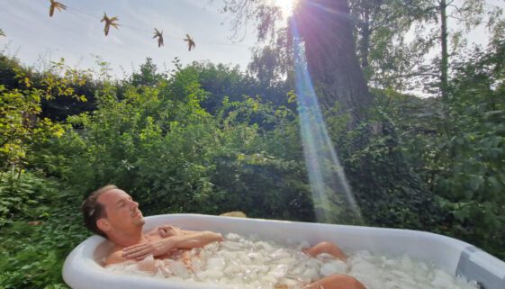 Een man ligt in een ijsbad midden in de natuur. De zon gaat achter hem onder